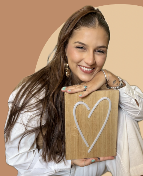 Taíssa Vanni sorrindo, apoiada em uma placa de madeira com um coração